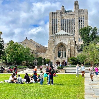 Groups of students hanging out on Cross Campus with Sterling Library in the background on a warm and sunny day.